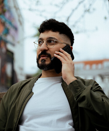 Junger Mann telefoniert im Freien. Er trägt eine grüne Jacke