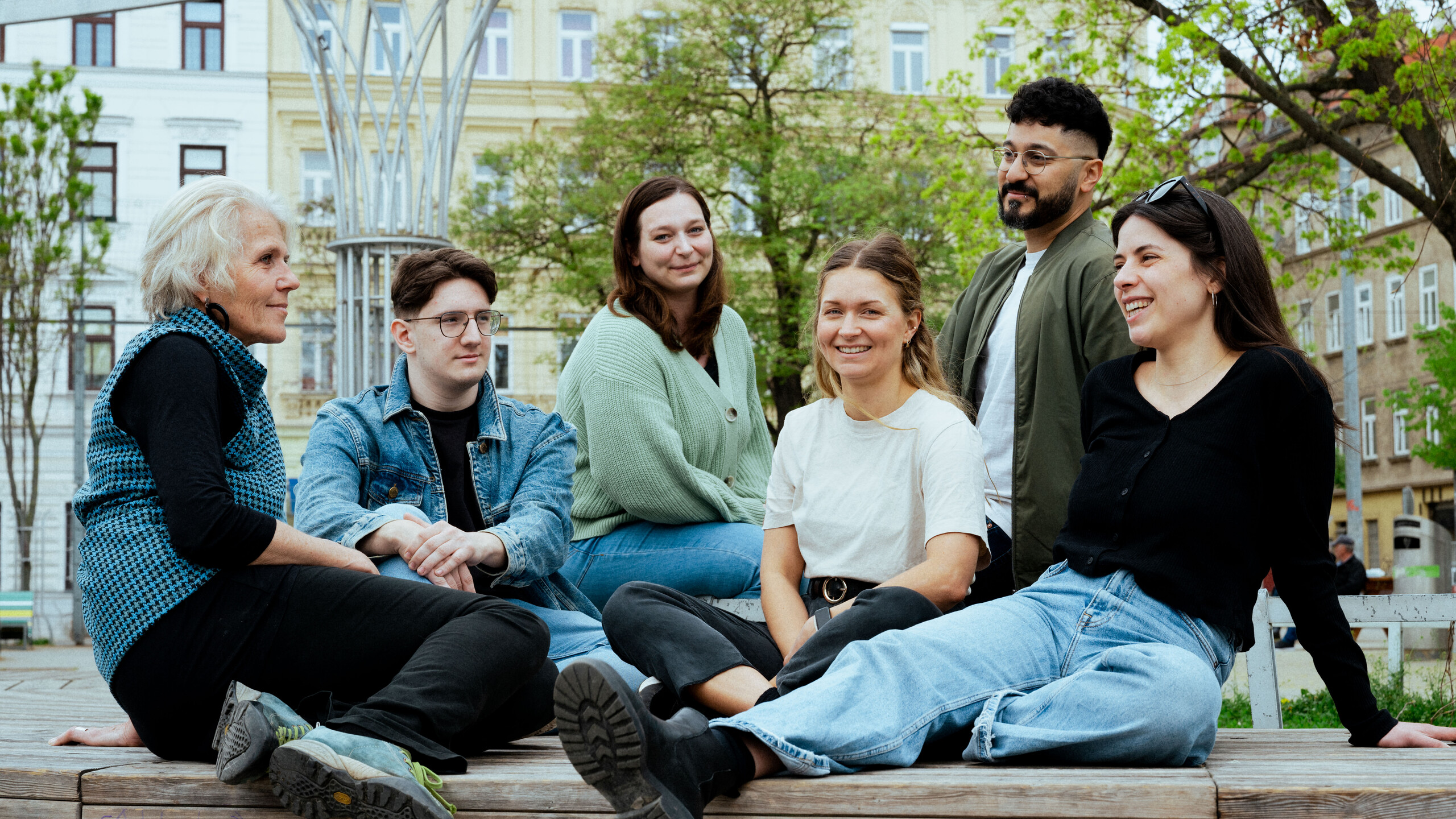 Sechs Menschen sitzen in einer Gruppe im Park zusammen und unterhalten sich